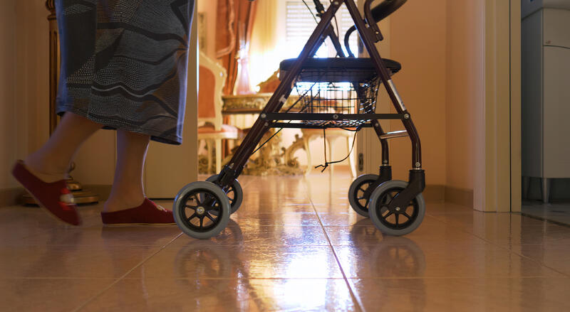 Elderly woman walks indoors with the walker. Detail of the legs