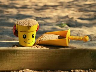 Illustrasjonsbilde: En spade og en liten kopp med sand på kanten av en sandkasse.