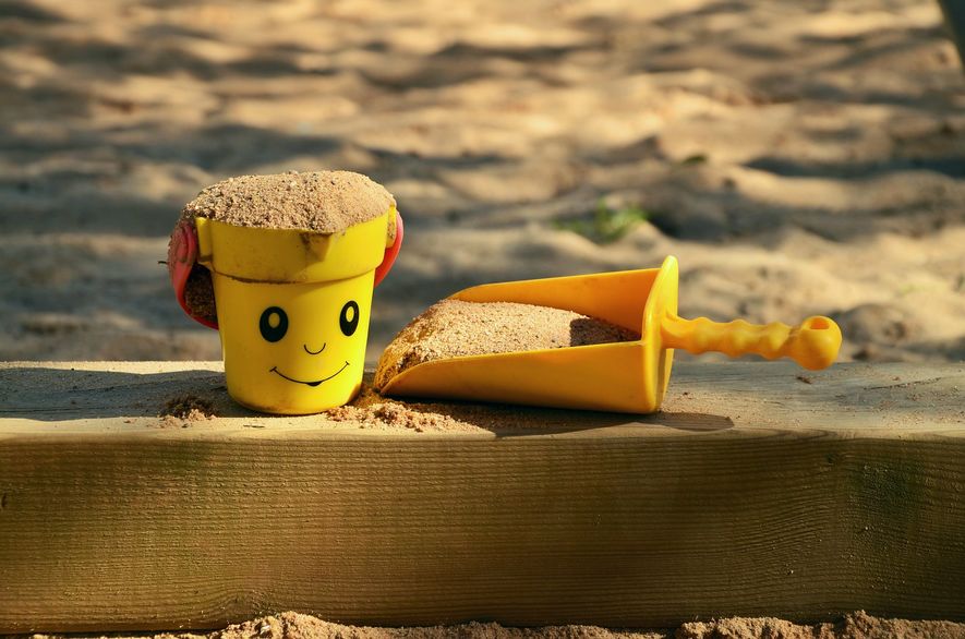Kommunens lekeplasser gjenåpner etter en periode hvor de har vært stengt som en del av koronatiltakene. Illustrasjonsbilde: En spade og en liten kopp med sand på kanten av en sandkasse.