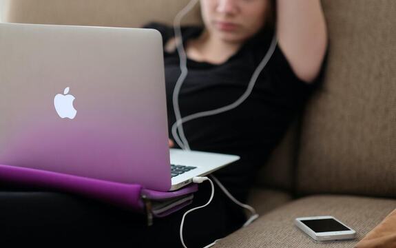 Ungdom i sofa med PC, telefon og ørepropper