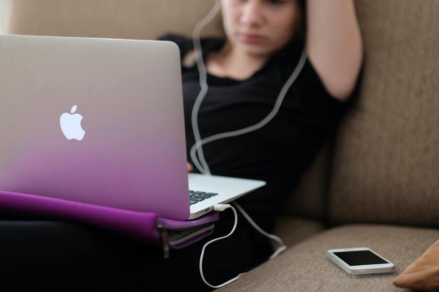Ungdom i sofa med PC, telefon og ørepropper