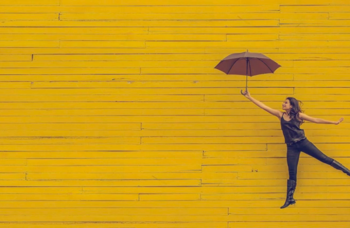 kvinne på ett ben med paraply gul bakgrunn