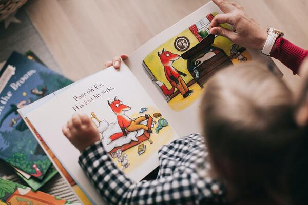 Bilde av et lite barn som sitter på et fang og leser i barnebok