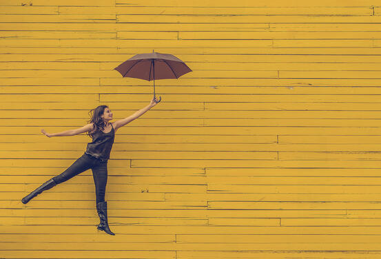 Dame med paraply mot gul vegg