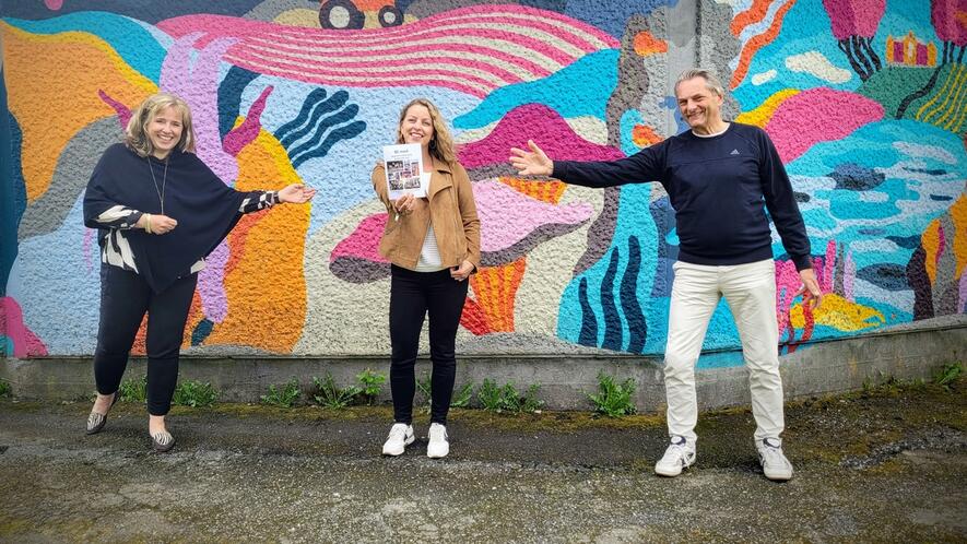 Foto av Vibeke, Monica og Alexander foran en fargerik vegg ved paviliongen i Ås sentrum