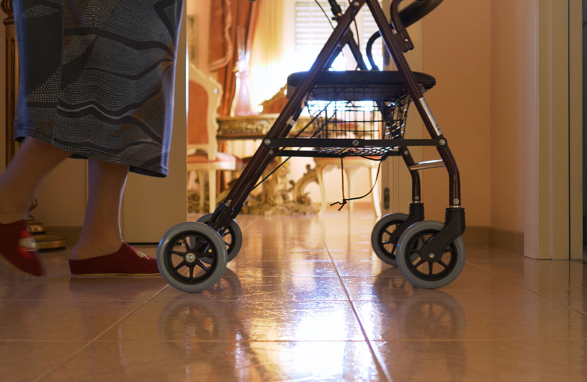 Elderly woman walks indoors with the walker. Detail of the legs