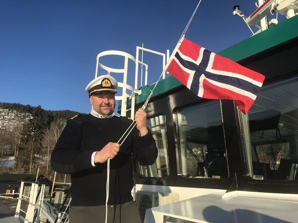 Bildet viser kaptein Roar Jønnes, som heiser flagget for å markere at den nye Randsfjordferja Elrond har blitt registrert som norsk fartøy. Foto: Aksel Aspeli