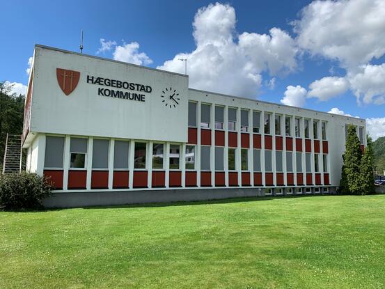 Kommunehuset i Hægebostad. Hvit murbygning med kommuneskjoldet og klokke