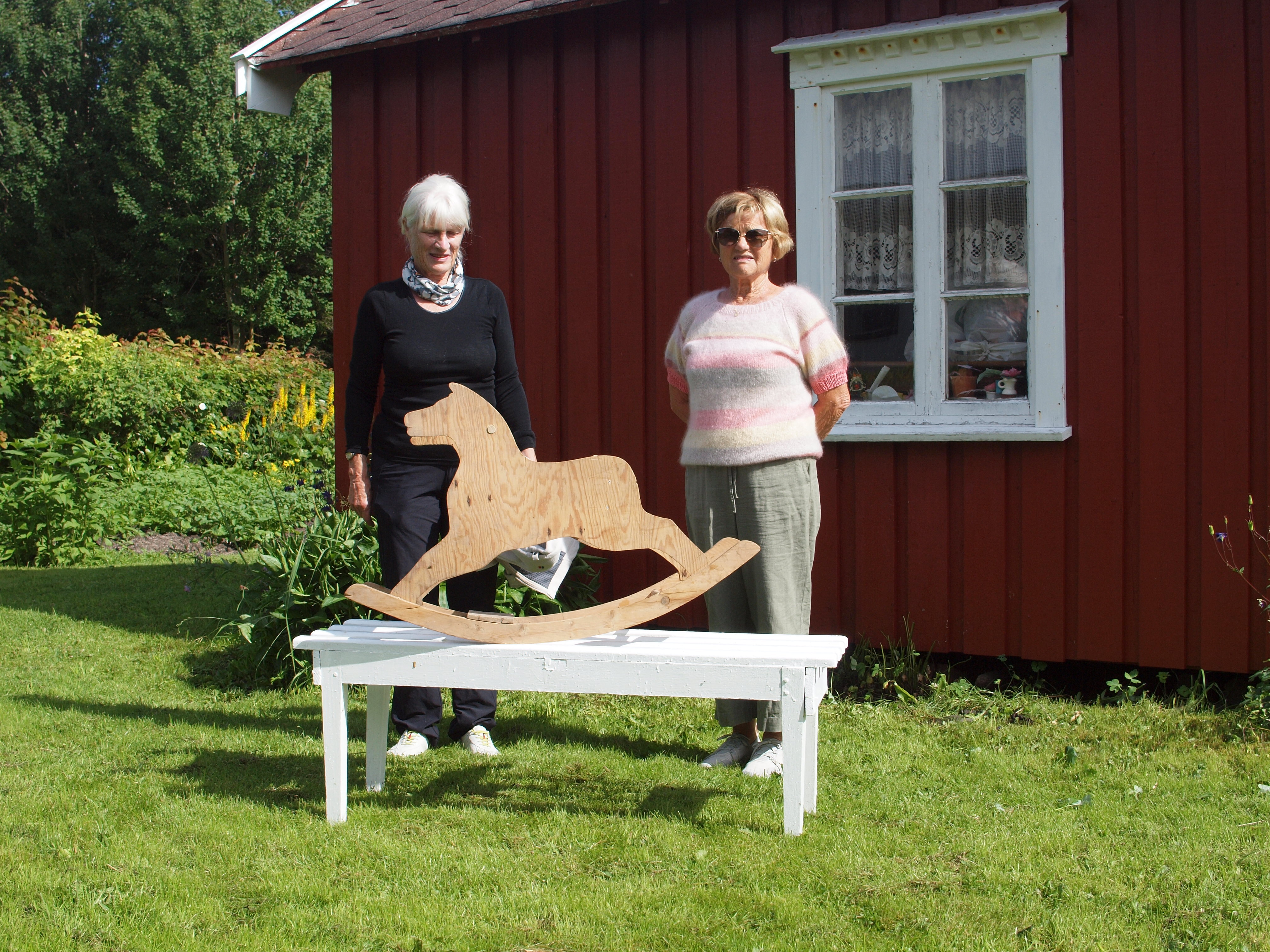Dagrunn Grønbech og Gerd G. Sjåvik med gyngehesten foran lekestua i barndomshagen på Tenna.