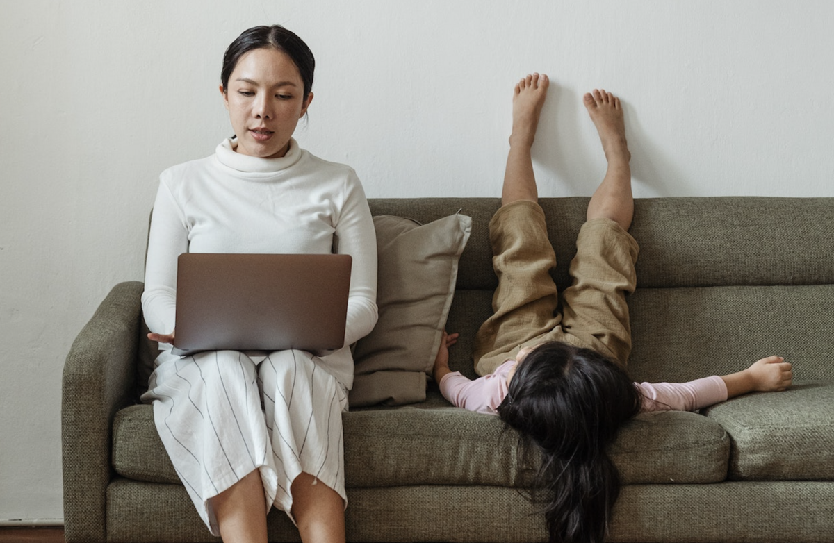 Kvinne med pc på fanget, barn opp ned i sofaen