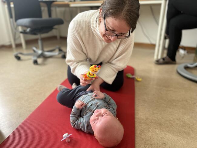Fysioterapeut Trude Røine-Elsrud har blikk-kontakt med en baby på gulvet