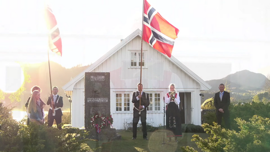 To mannlige flaggbærere i dress, en kvinnelig trompetist i bunad og to kvinner og en mann ved Pål Eikens bauta 17. mai 2020.