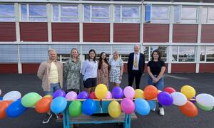 Skolegård med ballonger og ansatte som ønsker velkommen til skolestart