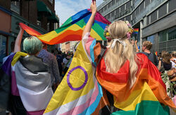 Pride 2023 i Oslo med regnbueflagg og fargerike personer sett bakfra.