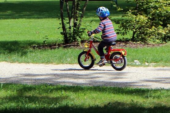 Gutt som sykler på rød sykkel langs en landeveg