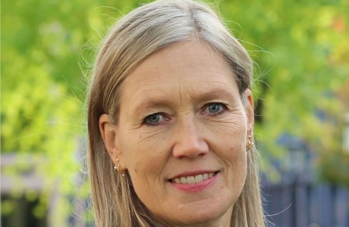 Kvinne med blå øyne og langt lyst hår. Grønn bakgrunn utenfor.