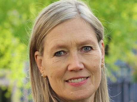 Kvinne med blå øyne og langt lyst hår. Grønn bakgrunn utenfor.