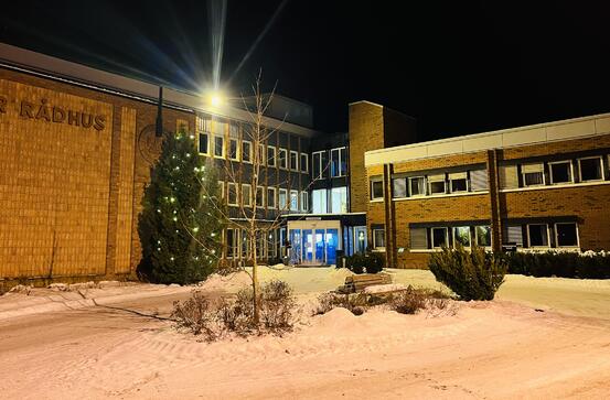 Bilde av inngangspartiet til rådhuset i kveldslys med juletre med lys foran.