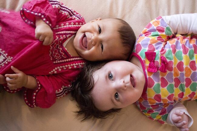 To babyer i fargerike klær som ligger på gulvet og smiler til kamera