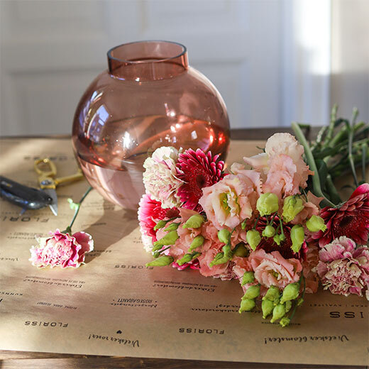 En flott bukett med tre ulike blomster i rosa- og ferskentoner innpakket i papir
