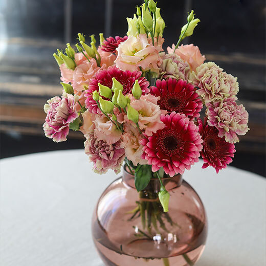 En flott bukett med tre ulike blomster i rosa- og ferskentoner i vase