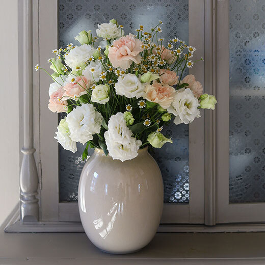 En flott bukett med tre ulike blomster i hvitt og ferskentoner i vase