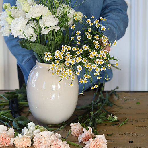 En flott bukett med tre ulike blomster i hvitt og ferskentoner settes i vase