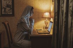Nonne sitter med en PC, sett fra siden