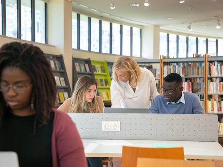 Tre kvinner og en mann på et bibliotek, sitter ved dataskjermer
