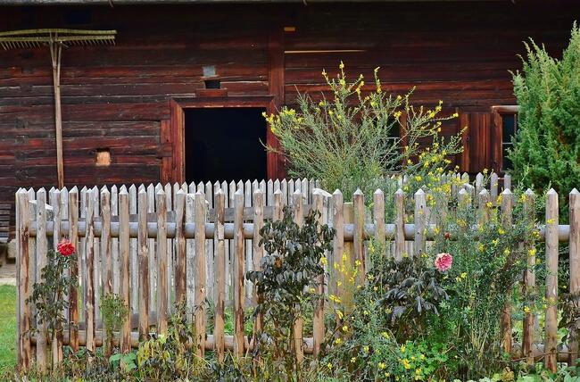 Deler av gammelt tømmerhus med gjerde med blomster foran