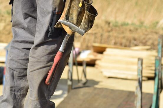 Utsnitt som viser ben til mann i arbeidsklær med en hammer som henger på buksa