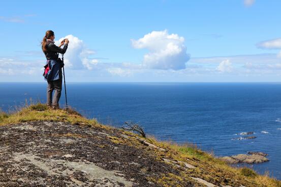 Bilde av dame på et berg som tar bilde av utsikten. Foto: Shutterstock