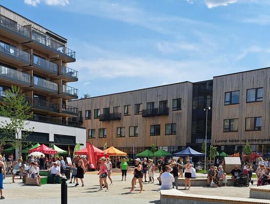 Bilde fra sommerfest 2023 som viser mangel folk på torget med noen som danser sumba i forgrunnen og med Lunner helse- og omsorgssenter i bakgrunnen