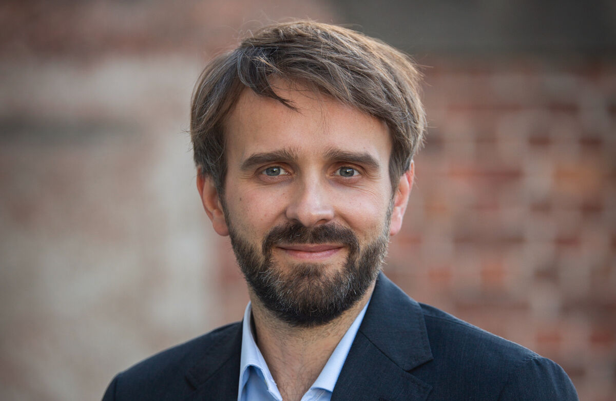 Jan Christian Vestre har skjegg og frakk. Murvegg, rødlig i bakgrunnen