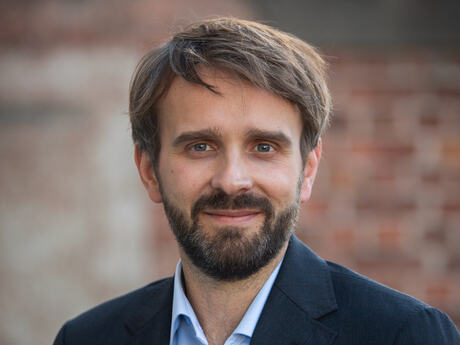 Jan Christian Vestre har skjegg og frakk. Murvegg, rødlig i bakgrunnen