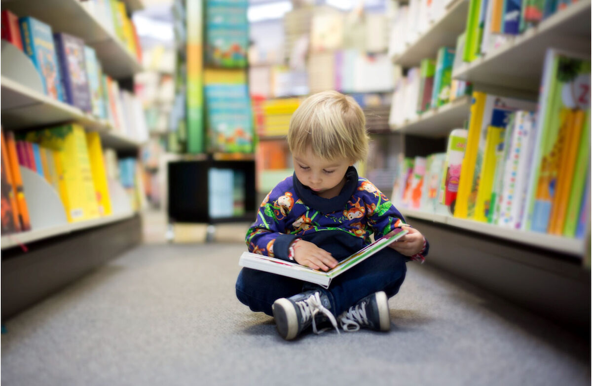 Barn på gulvet med bok på et bibliotek