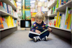 Barn på gulvet med bok på et bibliotek