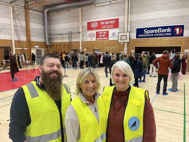 Representanter for de tre frivilligsentralene med gule vester i forgrunnen og folk som ser på kjoler i bakgrunnen. Lunnerhallen.