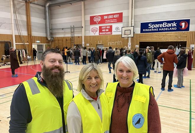 Representanter for de tre frivilligsentralene med gule vester i forgrunnen og folk som ser på kjoler i bakgrunnen. Lunnerhallen.