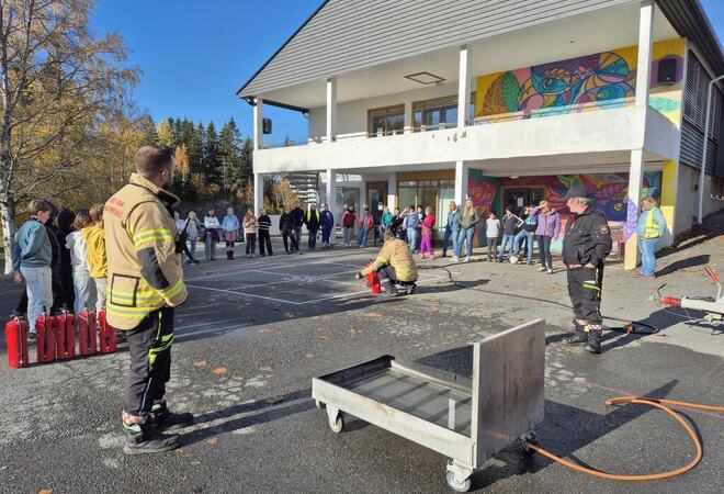 Barn utenfor skolen som ser på brannmenn demonstrerer slukningsustyr