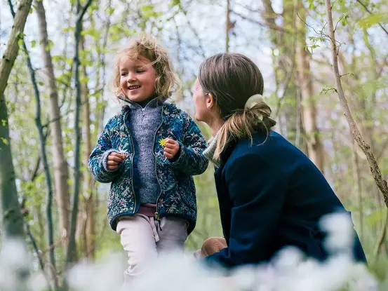 Liten jente med mor, ute i skogen. Moren ser på jenta som smiler stort.