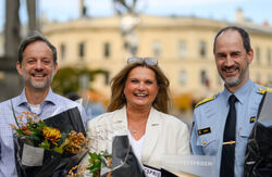 To menn og en kvinne, der hun står i midten. Alle tre har en blomsterbukett, og de smiler bredt.