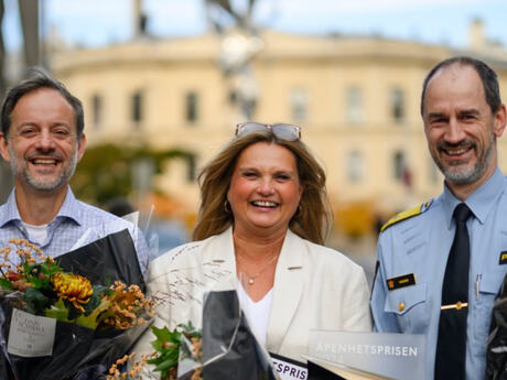 To menn og en kvinne, der hun står i midten. Alle tre har en blomsterbukett, og de smiler bredt.