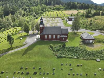 Bilde av Grua kirke sett ovenfra med kirkegården i forgrunnen. Bildet er tatt på sommeren.