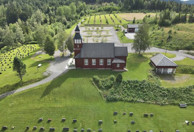 Bilde av Grua kirke sett ovenfra med kirkegården i forgrunnen. Bildet er tatt på sommeren.