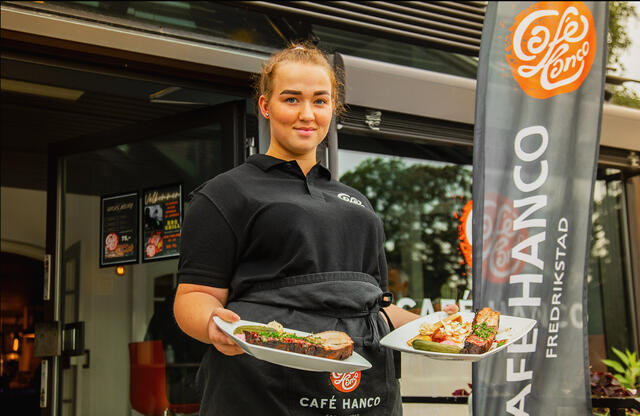 Bildet viser en ung kvinne utenfor Cafe Hanco, med en tallerken med mat i hver hånd.