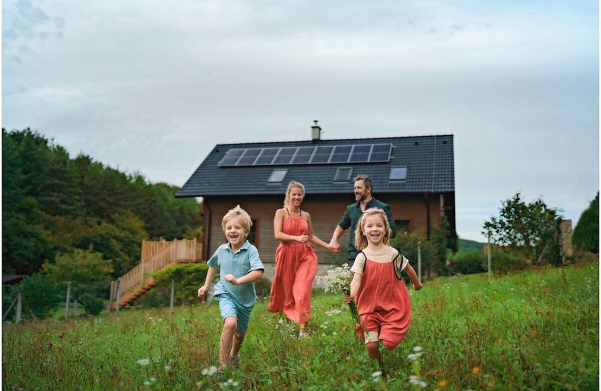 en lykkelig famile med en liten gutt og en jente foran og mor og far bak løper gjennom en eng med et hus i bakgrunnen.