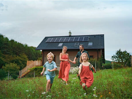 en lykkelig famile med en liten gutt og en jente foran og mor og far bak løper gjennom en eng med et hus i bakgrunnen.