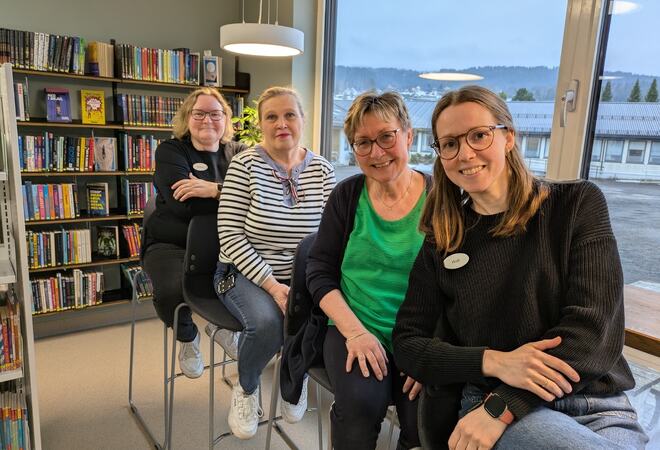 De fire ansatte på Lunner bibliotek på rekke og rad med bøker i bakgrunnen