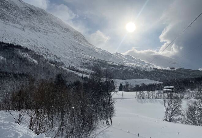 På bildet ser man en fjellside hvor det har gått et snøskred. Det er mye snø i området. Sola titter frem mellom skyene.